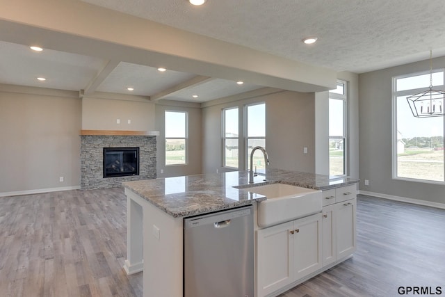 kitchen with light stone countertops, white cabinetry, sink, stainless steel dishwasher, and a center island with sink