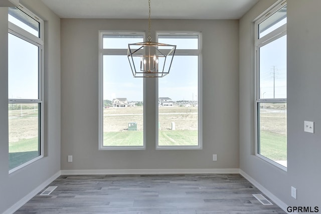 unfurnished dining area with hardwood / wood-style floors, a notable chandelier, and a wealth of natural light