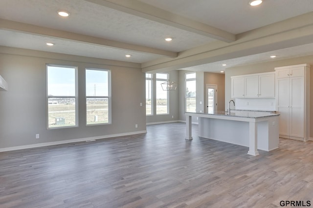 interior space featuring beam ceiling, a kitchen island with sink, white cabinets, and light hardwood / wood-style floors