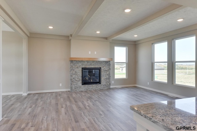 unfurnished living room featuring a stone fireplace, light hardwood / wood-style flooring, beamed ceiling, and a textured ceiling