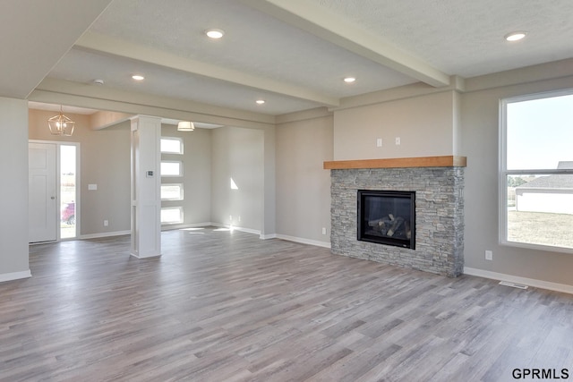 unfurnished living room featuring beamed ceiling, a textured ceiling, light hardwood / wood-style flooring, and a stone fireplace