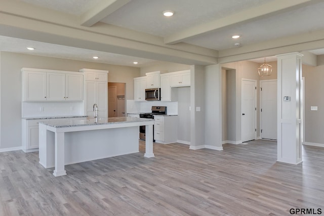 kitchen with beam ceiling, light stone counters, a center island with sink, white cabinets, and appliances with stainless steel finishes