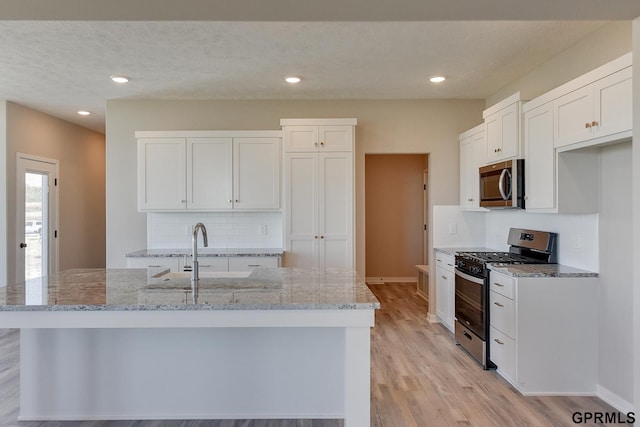 kitchen featuring light stone counters, white cabinets, an island with sink, and appliances with stainless steel finishes