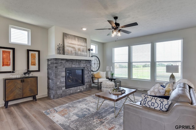 living room with a fireplace, light wood-type flooring, a textured ceiling, and ceiling fan