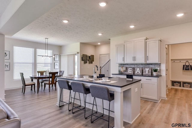 kitchen featuring white cabinetry, light hardwood / wood-style floors, a textured ceiling, decorative light fixtures, and a center island with sink