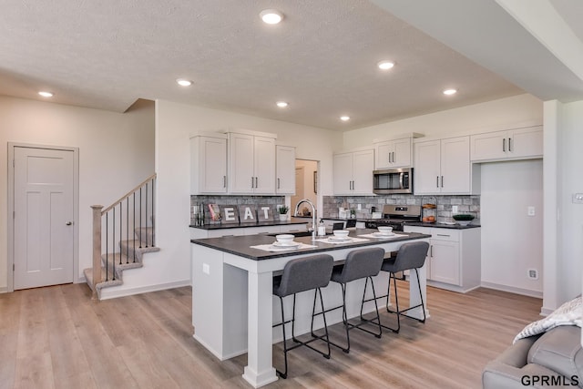 kitchen with white cabinets, a breakfast bar, a center island with sink, and appliances with stainless steel finishes