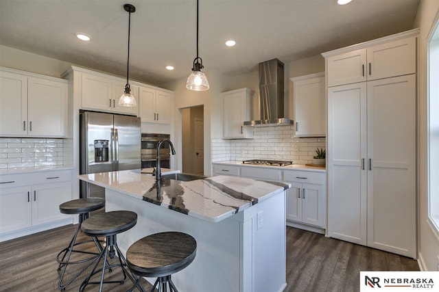 kitchen with white cabinets, a kitchen island with sink, hanging light fixtures, and wall chimney range hood