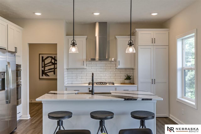 kitchen with wall chimney exhaust hood, stainless steel appliances, tasteful backsplash, pendant lighting, and white cabinets