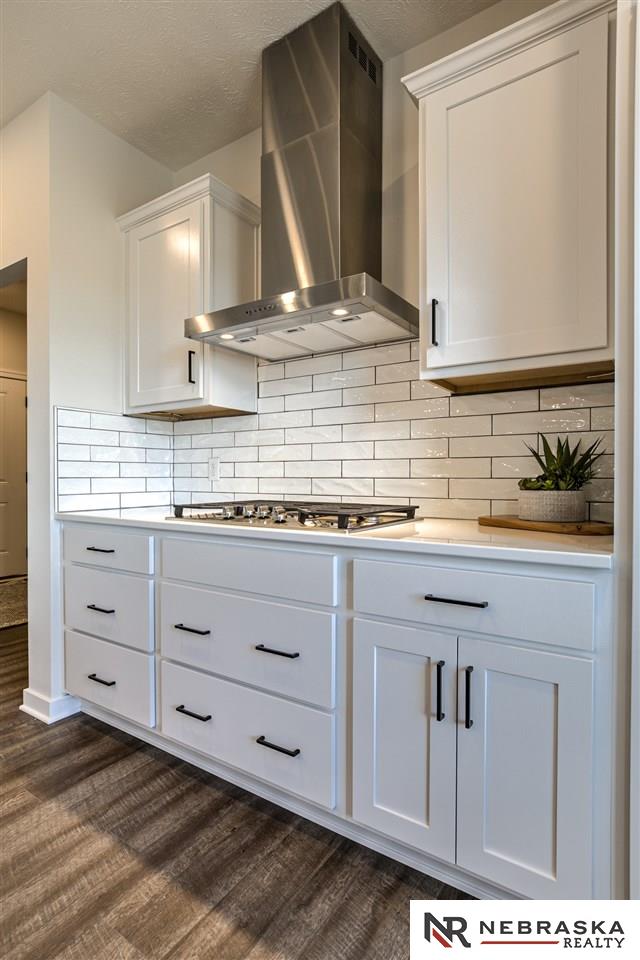 kitchen featuring white cabinets, wall chimney exhaust hood, backsplash, and dark wood-type flooring