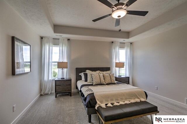 bedroom featuring ceiling fan, multiple windows, and a tray ceiling