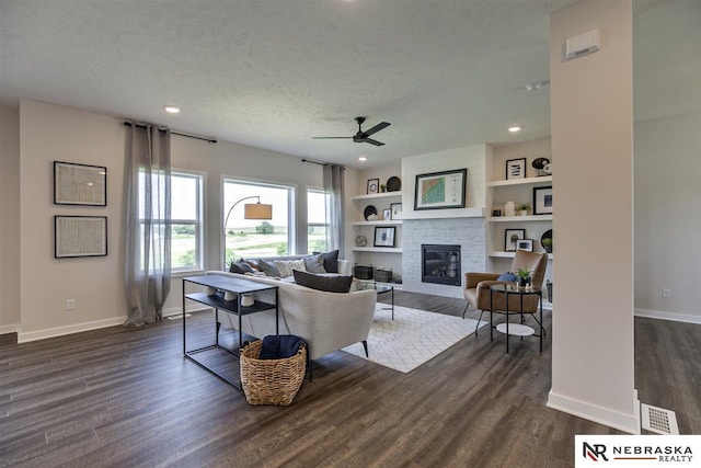 living room with ceiling fan, a fireplace, built in features, and a textured ceiling