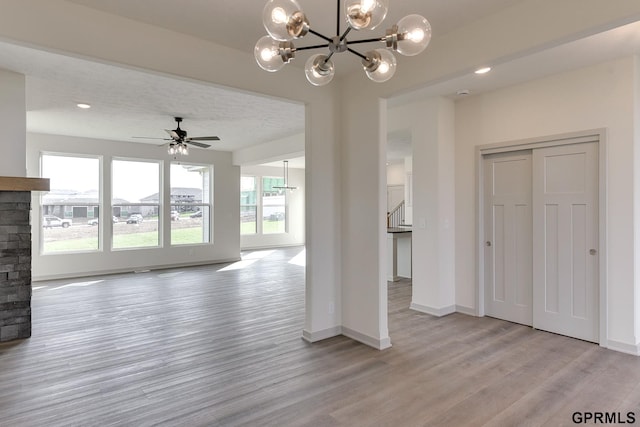 unfurnished living room with ceiling fan with notable chandelier, light hardwood / wood-style floors, a stone fireplace, and a wealth of natural light