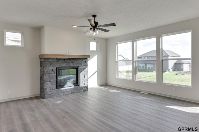 unfurnished living room with a stone fireplace, ceiling fan, and light hardwood / wood-style flooring