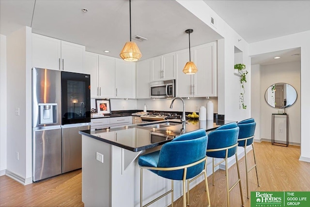 kitchen featuring pendant lighting, light hardwood / wood-style floors, a breakfast bar area, white cabinets, and appliances with stainless steel finishes