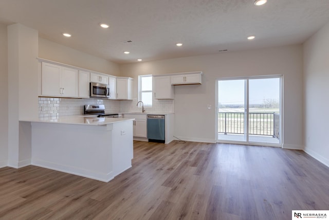 kitchen with light hardwood / wood-style flooring, decorative backsplash, white cabinetry, kitchen peninsula, and stainless steel appliances