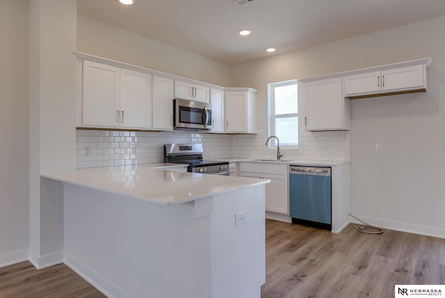 kitchen with kitchen peninsula, appliances with stainless steel finishes, white cabinetry, and sink