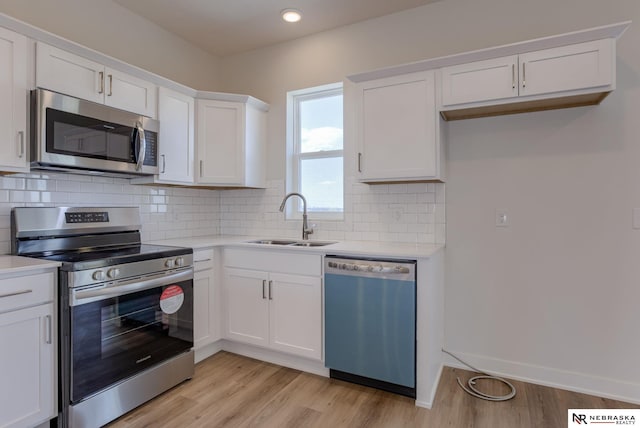 kitchen with appliances with stainless steel finishes, light wood-type flooring, tasteful backsplash, sink, and white cabinets