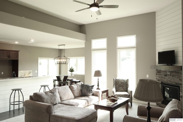 living room featuring a stone fireplace and ceiling fan with notable chandelier