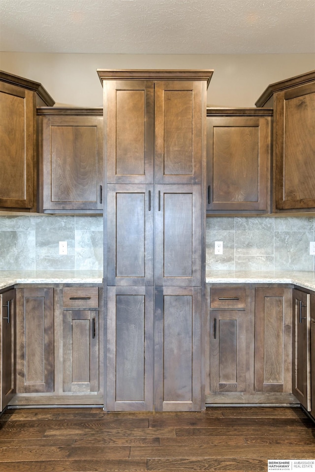 kitchen featuring decorative backsplash, dark hardwood / wood-style flooring, light stone counters, and a textured ceiling