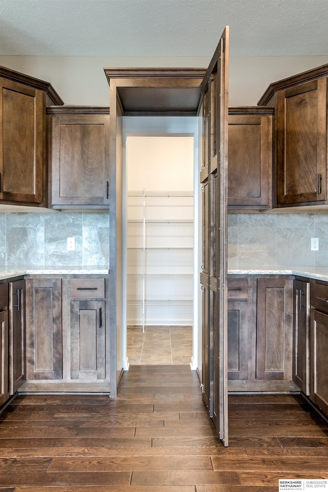 kitchen with dark brown cabinets, dark hardwood / wood-style flooring, and tasteful backsplash