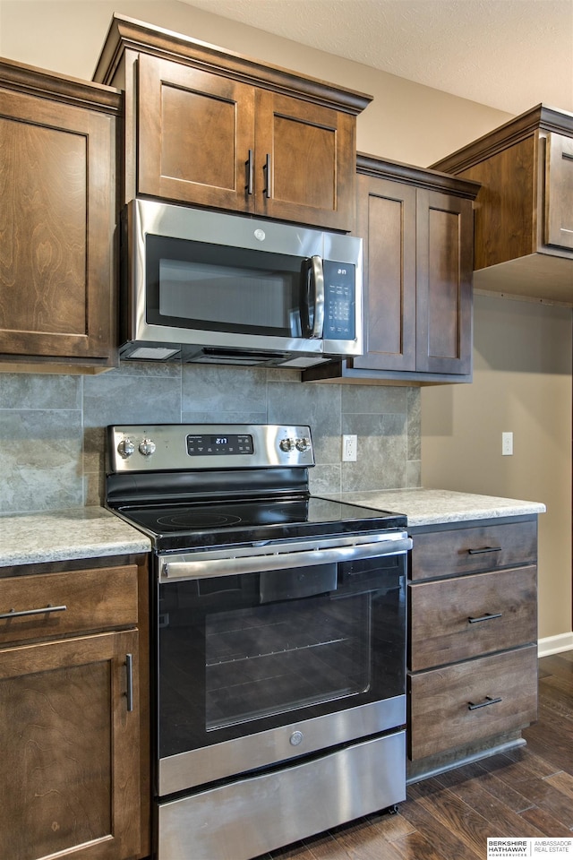 kitchen with appliances with stainless steel finishes, dark hardwood / wood-style flooring, and backsplash