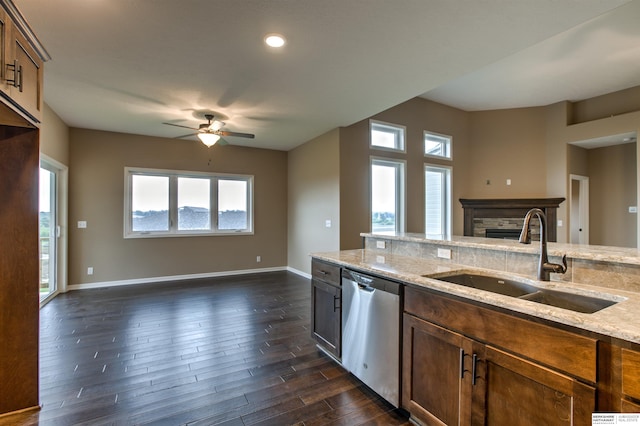 kitchen featuring light stone counters, a fireplace, ceiling fan, sink, and dishwasher