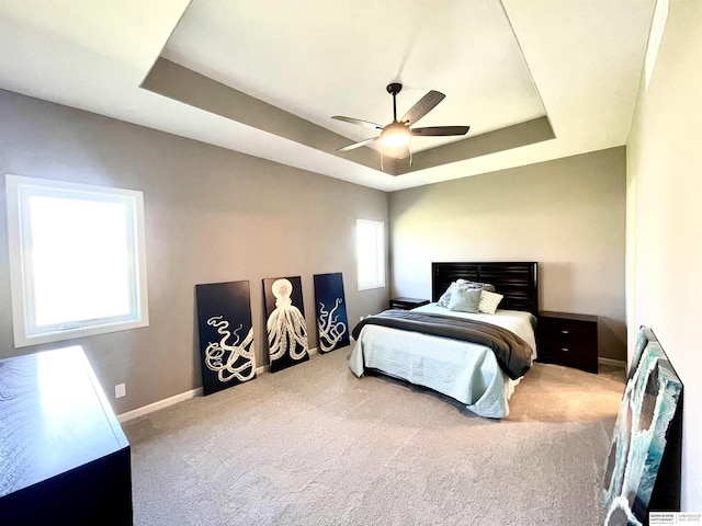 carpeted bedroom with a tray ceiling and ceiling fan