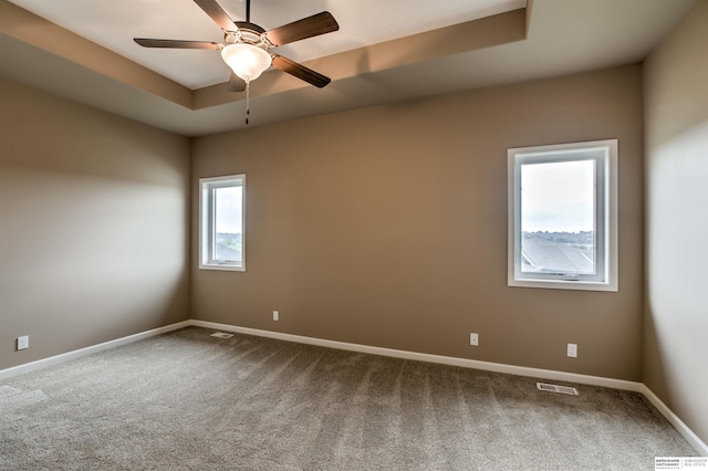 empty room featuring carpet, ceiling fan, and a raised ceiling