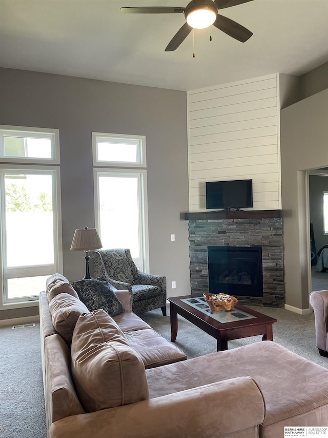 carpeted living room featuring ceiling fan and a stone fireplace