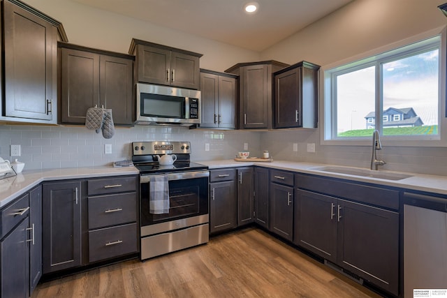 kitchen with appliances with stainless steel finishes, backsplash, dark brown cabinets, sink, and light hardwood / wood-style flooring