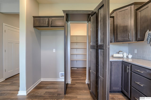 kitchen with dark brown cabinets, dark hardwood / wood-style floors, light stone counters, and backsplash