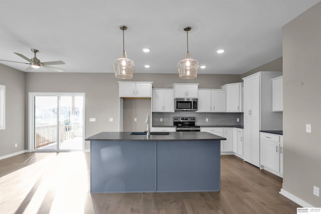 kitchen with stainless steel appliances, a kitchen island with sink, sink, pendant lighting, and white cabinets