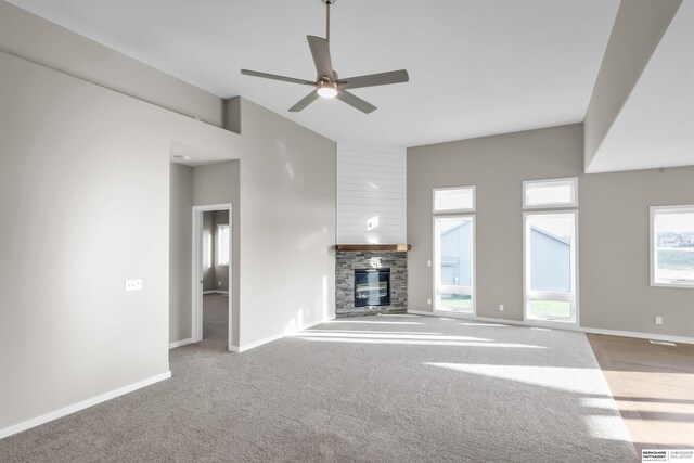 unfurnished living room with ceiling fan, a fireplace, light carpet, and a high ceiling