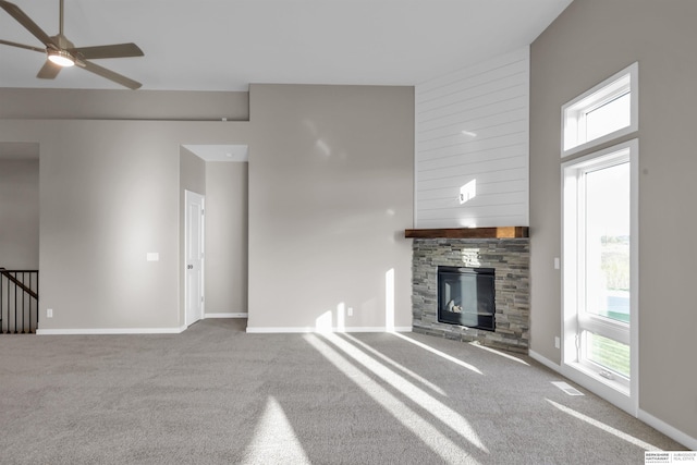 unfurnished living room with carpet flooring, a towering ceiling, a stone fireplace, and ceiling fan