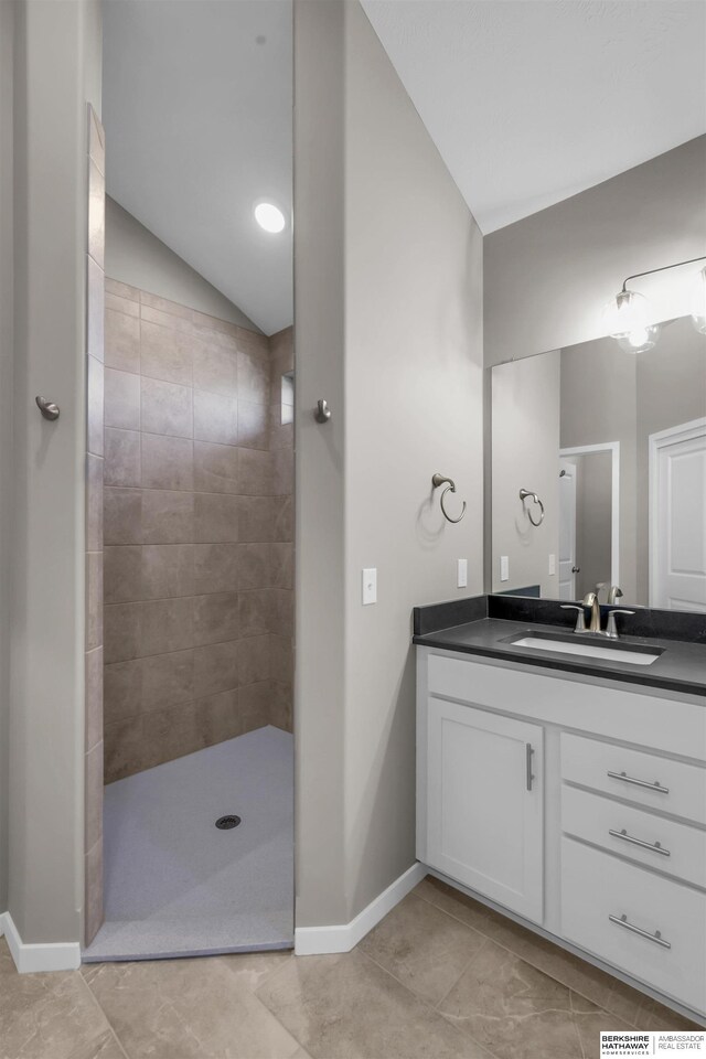 bathroom featuring tile patterned flooring, a tile shower, vanity, and vaulted ceiling