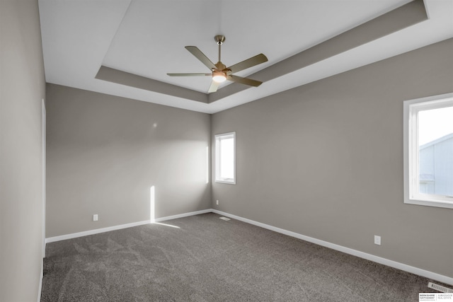 empty room with a raised ceiling, ceiling fan, and carpet floors