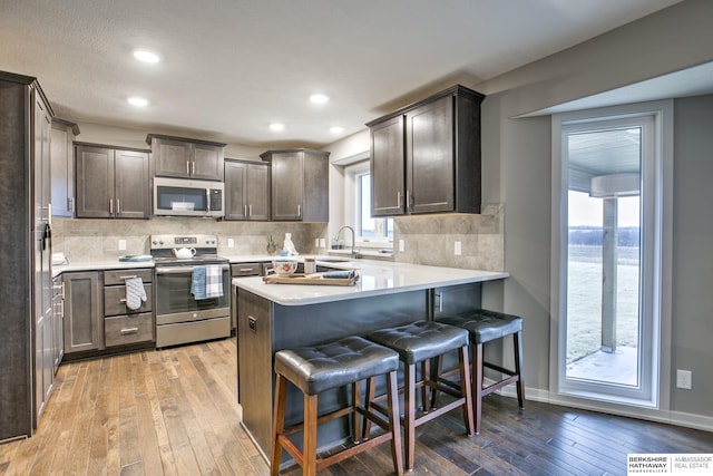 kitchen with a kitchen bar, appliances with stainless steel finishes, dark brown cabinetry, and light hardwood / wood-style floors