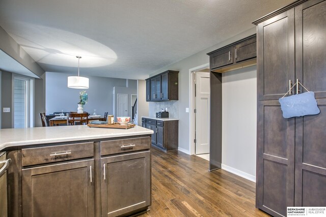 kitchen featuring dark brown cabinets, dark hardwood / wood-style floors, stainless steel dishwasher, and pendant lighting