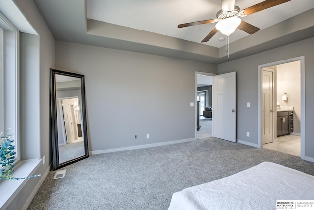 carpeted bedroom with a tray ceiling, ceiling fan, and ensuite bathroom