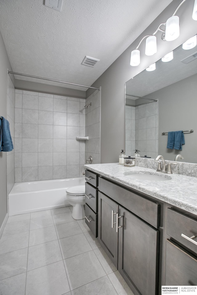 full bathroom with vanity, tile patterned flooring, tiled shower / bath combo, toilet, and a textured ceiling