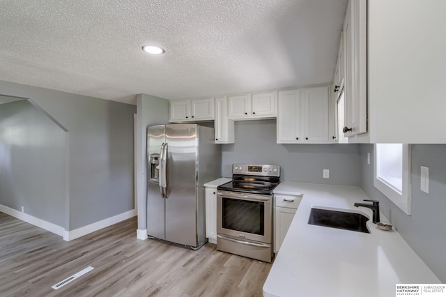 kitchen featuring a textured ceiling, stainless steel appliances, sink, light hardwood / wood-style floors, and white cabinetry