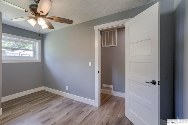 unfurnished bedroom featuring ceiling fan, light wood-type flooring, and a textured ceiling