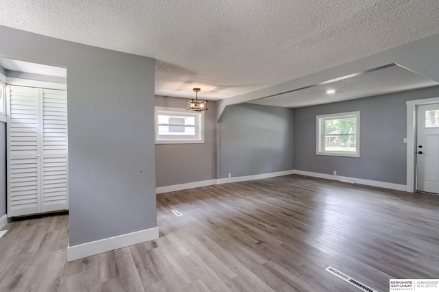 spare room featuring plenty of natural light, light wood-type flooring, and an inviting chandelier