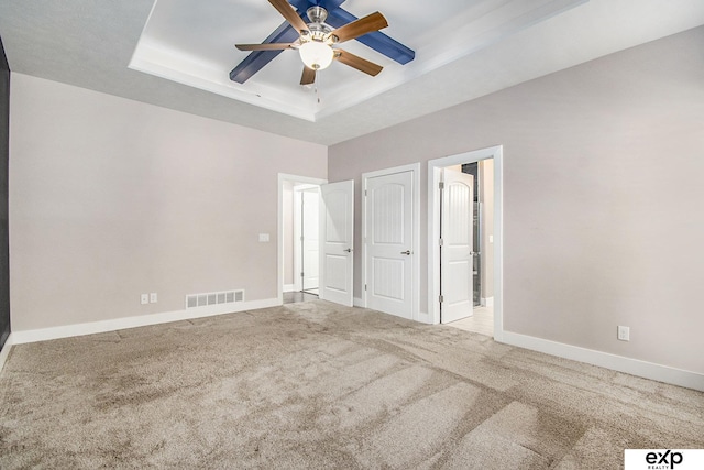 unfurnished bedroom featuring light carpet, a tray ceiling, and ceiling fan