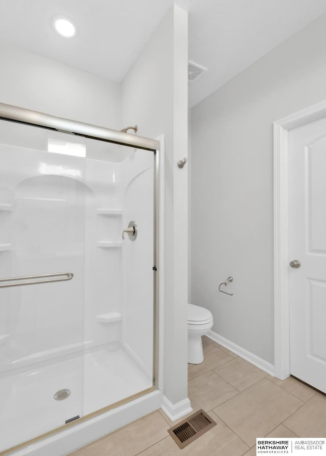 bathroom featuring toilet, tile patterned flooring, and a shower with shower door