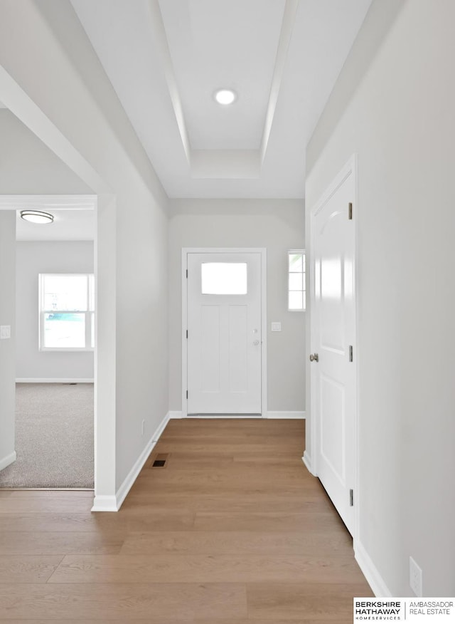 doorway featuring light wood-type flooring and a tray ceiling