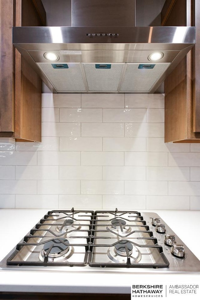 interior details featuring stainless steel gas stovetop, decorative backsplash, and wall chimney range hood