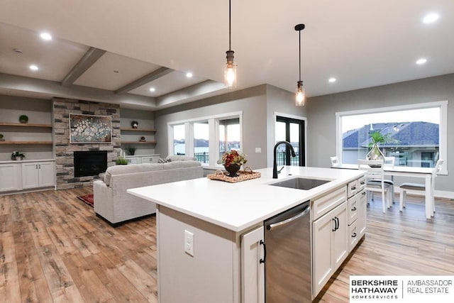 kitchen featuring stainless steel dishwasher, sink, white cabinets, hanging light fixtures, and an island with sink