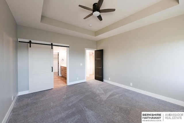 unfurnished bedroom featuring a tray ceiling, a barn door, ensuite bathroom, and ceiling fan