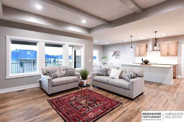 living room featuring a healthy amount of sunlight, beamed ceiling, and light hardwood / wood-style floors